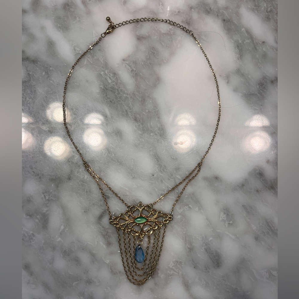 Gold necklace with green and blue gem on it